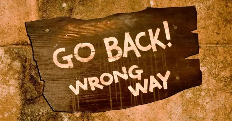 A close up of a wooden sign on a brick wall that reads 'Go Back! Wrong way.'