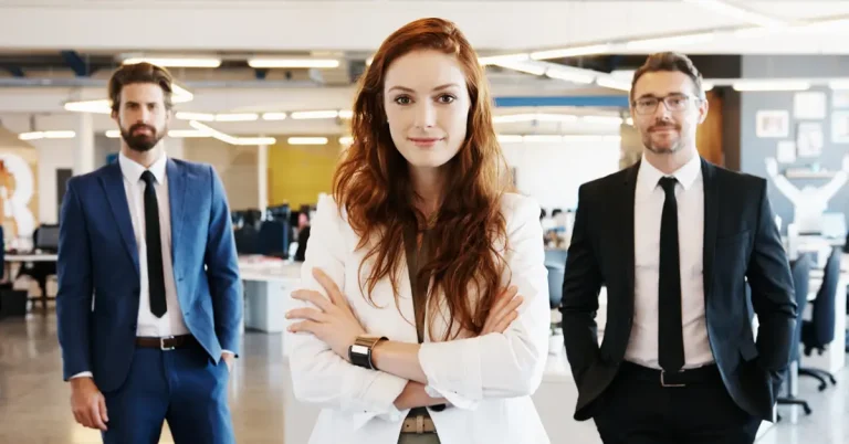 Three smartly dressed office workers posing for a portrait in a large open-plan office.